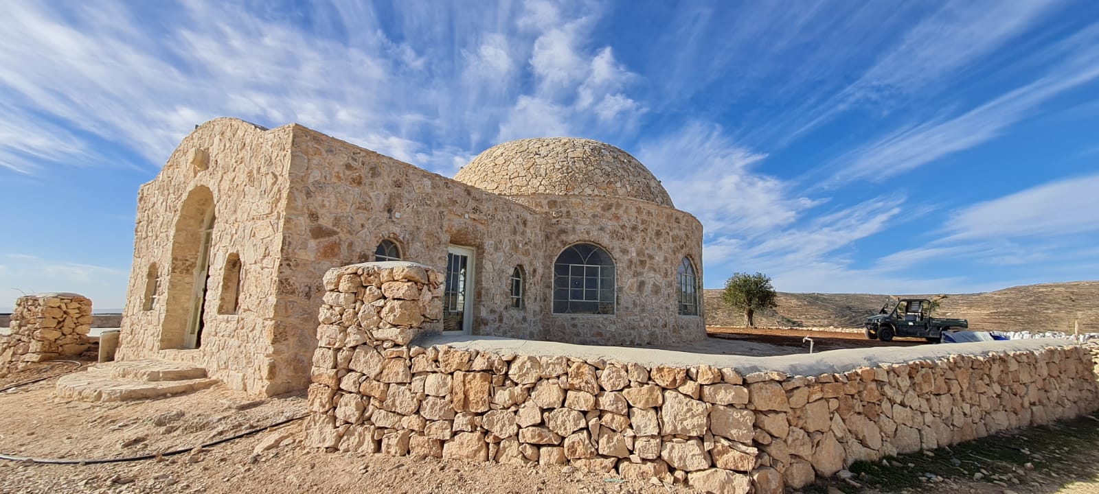 Stone walls and domed prayer house at Arugot Spiritual Center beneath a blue sky